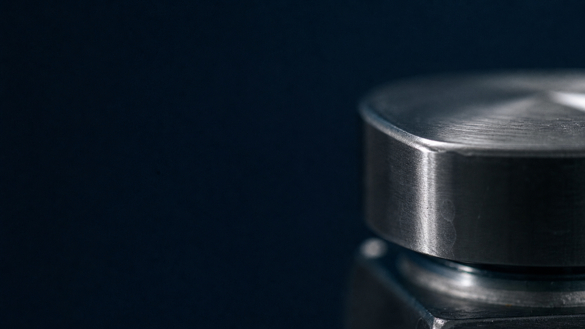 Macro detail of a brushed stainless valve handle on Inquivix Technologies equipment, photographed against a deep navy background